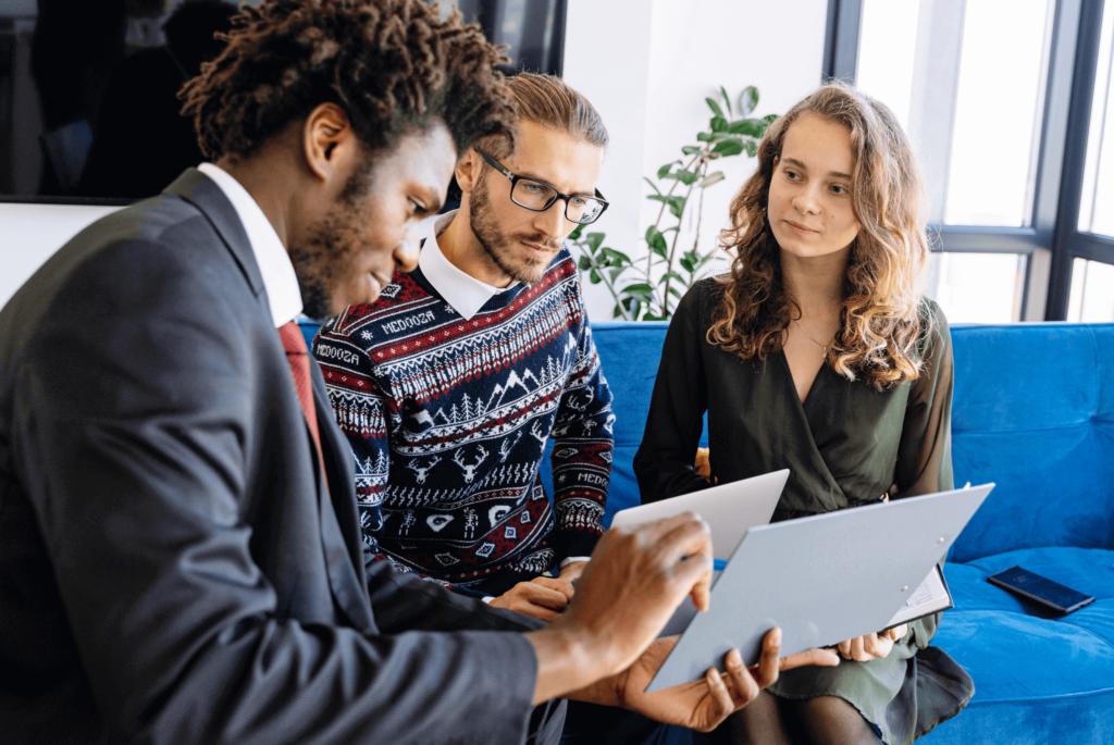 Three professionals discussing property management strategies, showcasing collaboration to maximize profits in commercial real estate, with laptops and documents on a blue couch.