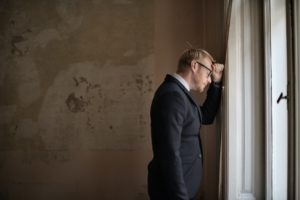 Man in a suit looking out of a window, appearing contemplative or distressed, reflecting the challenges of property management and evictions.