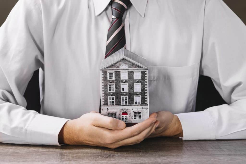 Man in a dress shirt and tie holding a miniature house, symbolizing property investment and financial planning for rental real estate investors.