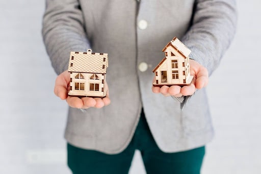 Person holding two wooden model houses in hands, representing property management and branding for rental properties.