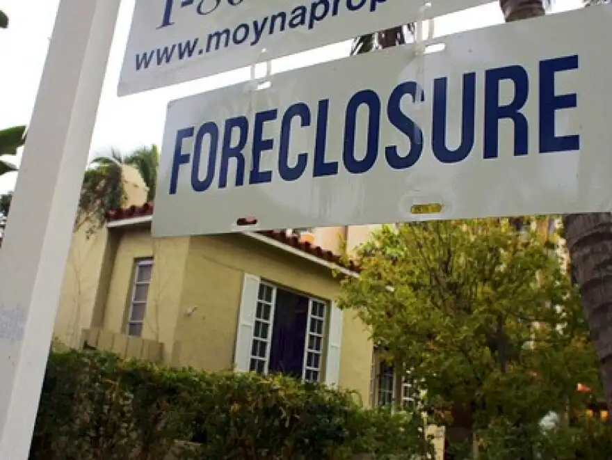 Foreclosure sign in front of a house with greenery and trees in the background during daytime.